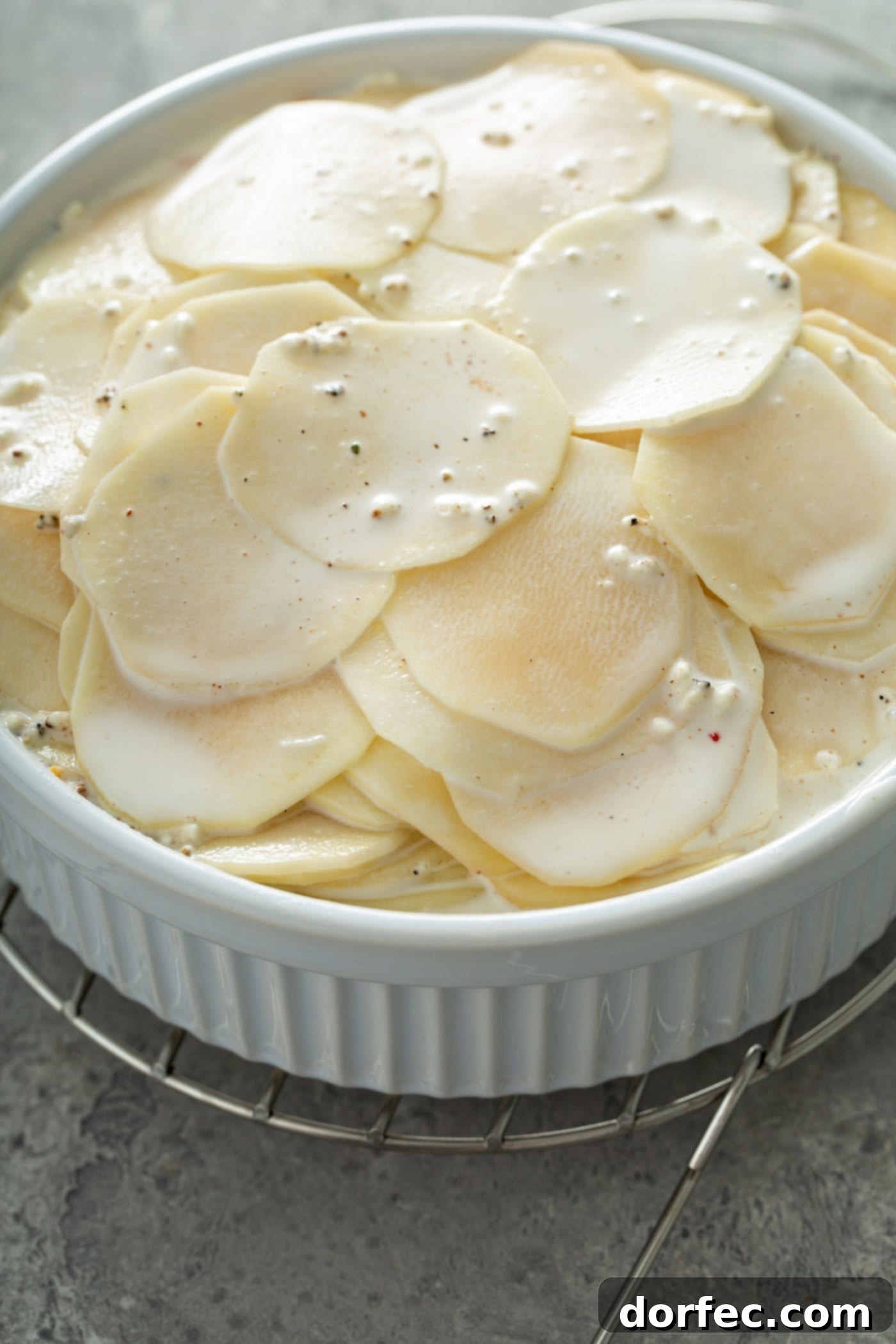 A casserole dish filled with sliced raw potatoes. A cream sauce is poured over the top.