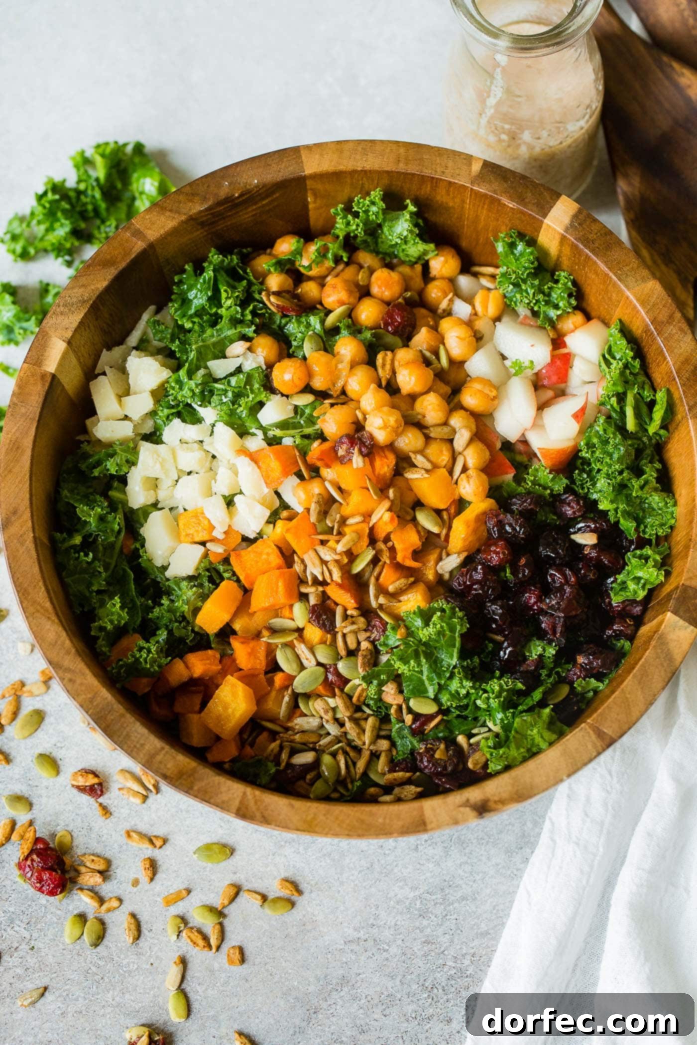 Golden Roasted Butternut & Kale Power Salad 2 A photo of a large wooden bowl full of kale salad topped with roasted butternut squash, craisins, chickpeas, pepitas, apples and gouda cheese.