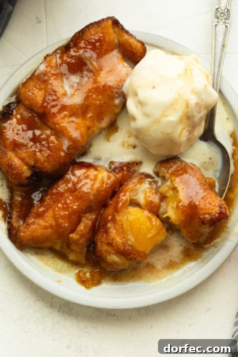 A small dessert plate with three golden baked peach dumplings, beautifully golden brown, topped with a melting scoop of creamy vanilla ice cream, creating a perfect balance of warm and cool textures.