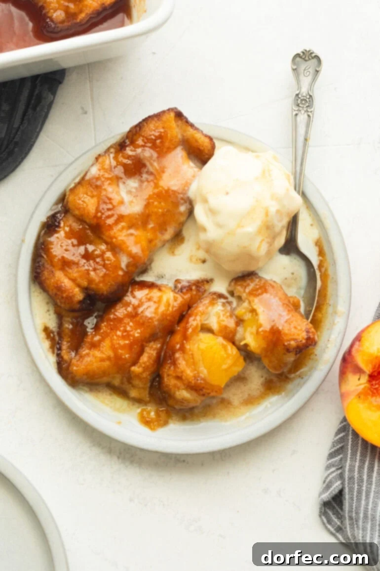 Three golden baked peach dumplings with crescent rolls, invitingly arranged with a generous scoop of vanilla ice cream melting softly on top, and a spoon gently scooping into one of the dumplings, showcasing its tender interior.