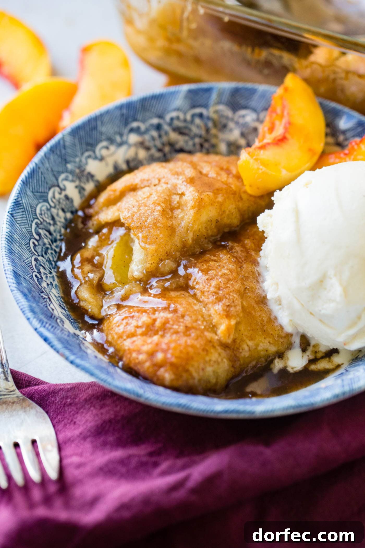 A beautiful blue dish on a soft purple napkin, holding two perfectly baked peach dumplings and a generous scoop of creamy vanilla ice cream, a delightful sweet treat.