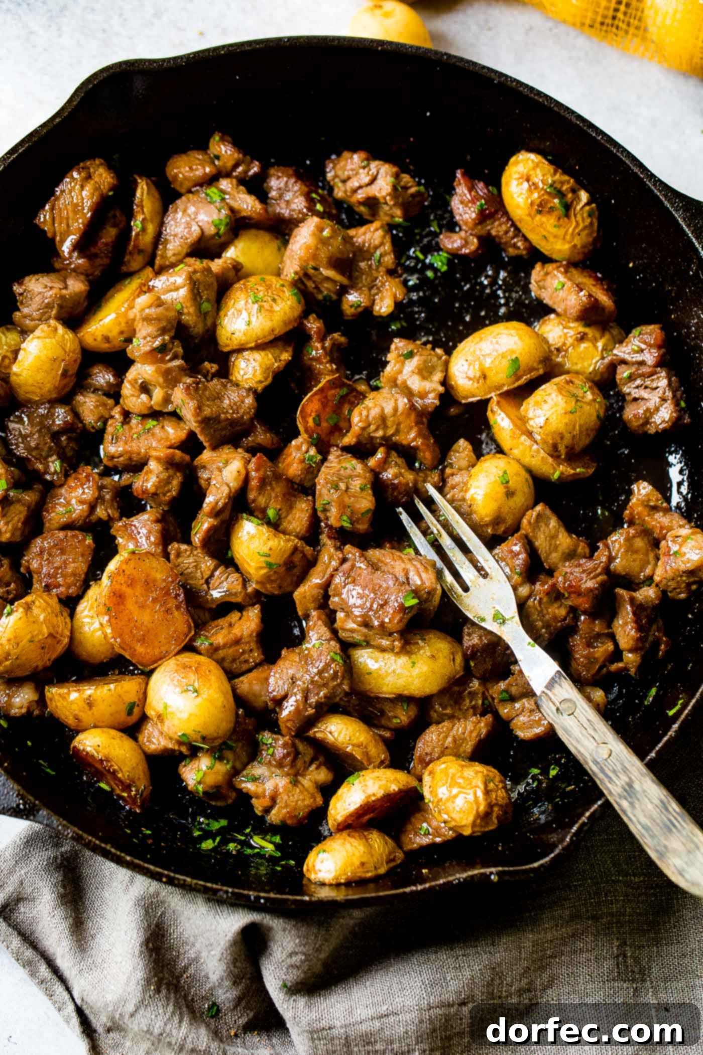 A photo of a cast iron skillet full of smoky steak and potatoes, showing the beautiful sear on the meat.