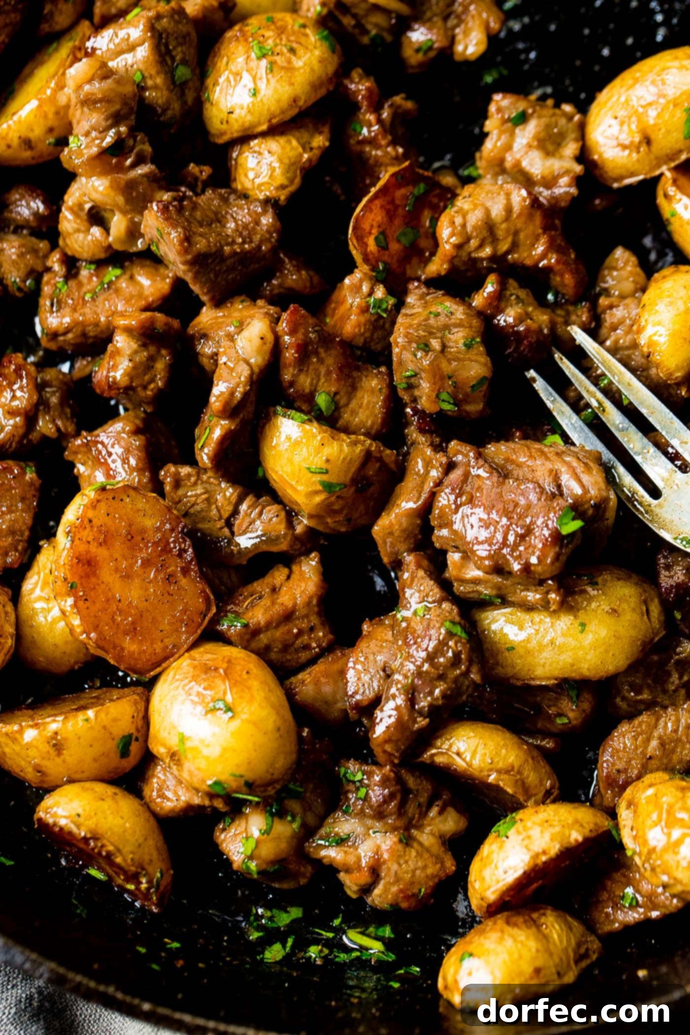 A photo of a cast iron skillet full of golden halved potatoes and beautifully seared steak, ready to be served for dinner.