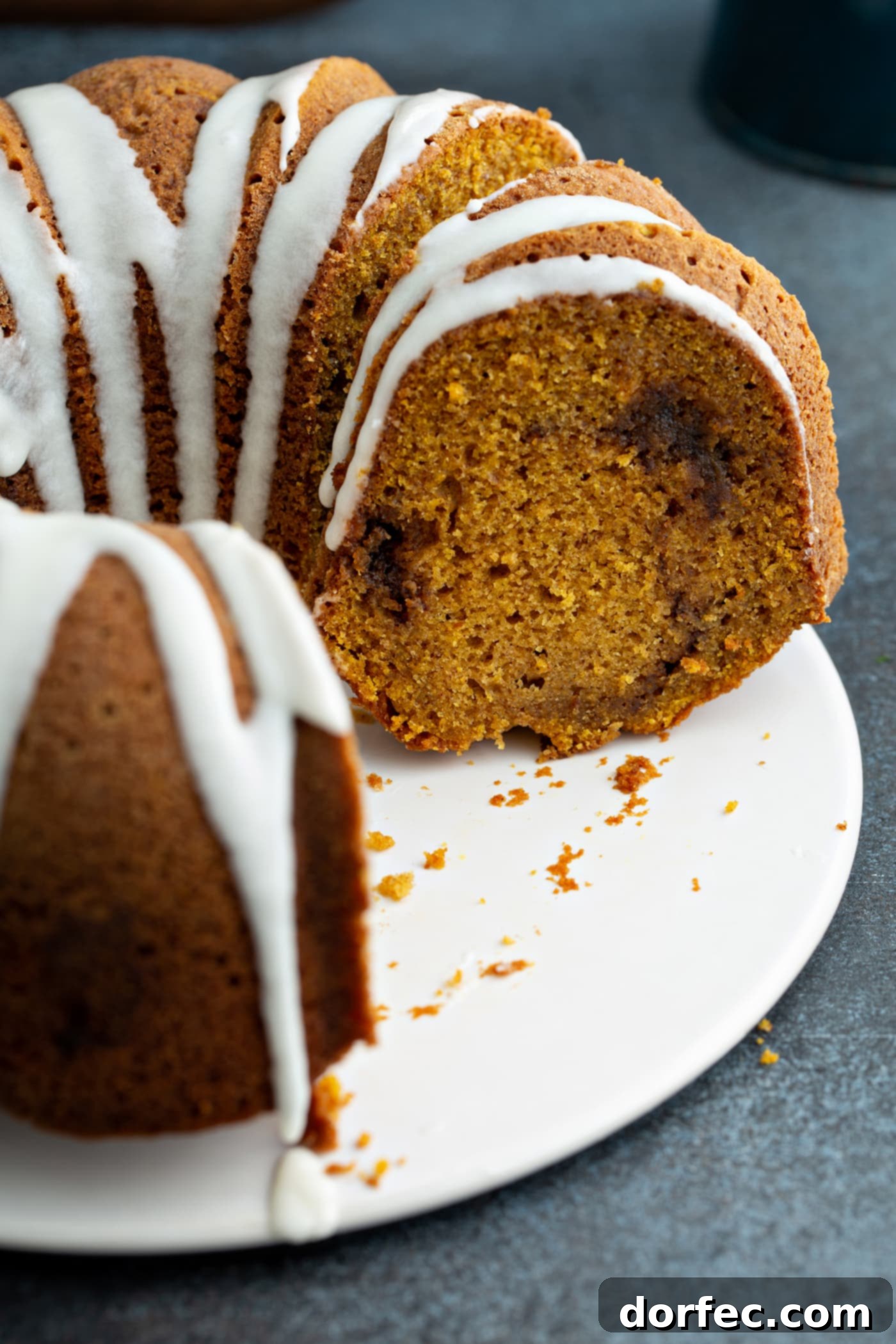 Sour Cream Cinnamon Swirl Pumpkin Bundt Cake A sour cream cinnamon swirl pumpkin bundt cake with a few slices removed. The cake is drizzled with white glaze and you can see the cinnamon swirl in the middle of the cake.