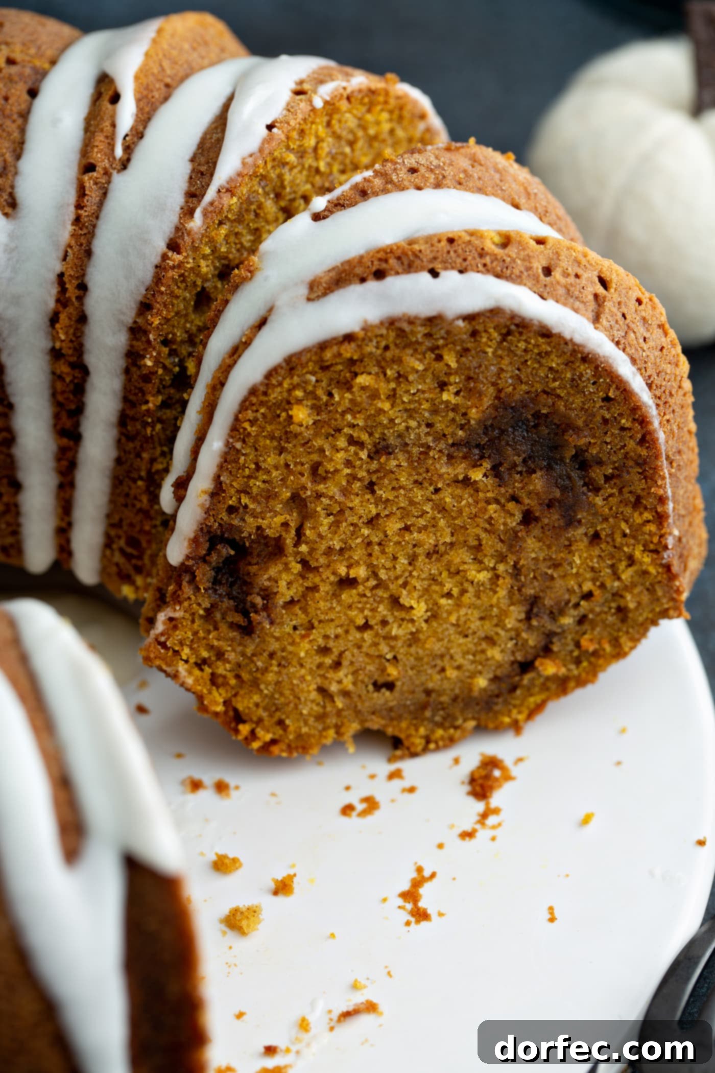 Sour Cream Cinnamon Swirl Pumpkin Bundt Cake A close-up picture of a sliced sour cream cinnamon swirl pumpkin bundt cake. The cake is drizzled with white glaze and you can see the cinnamon swirl in the middle of the cake.