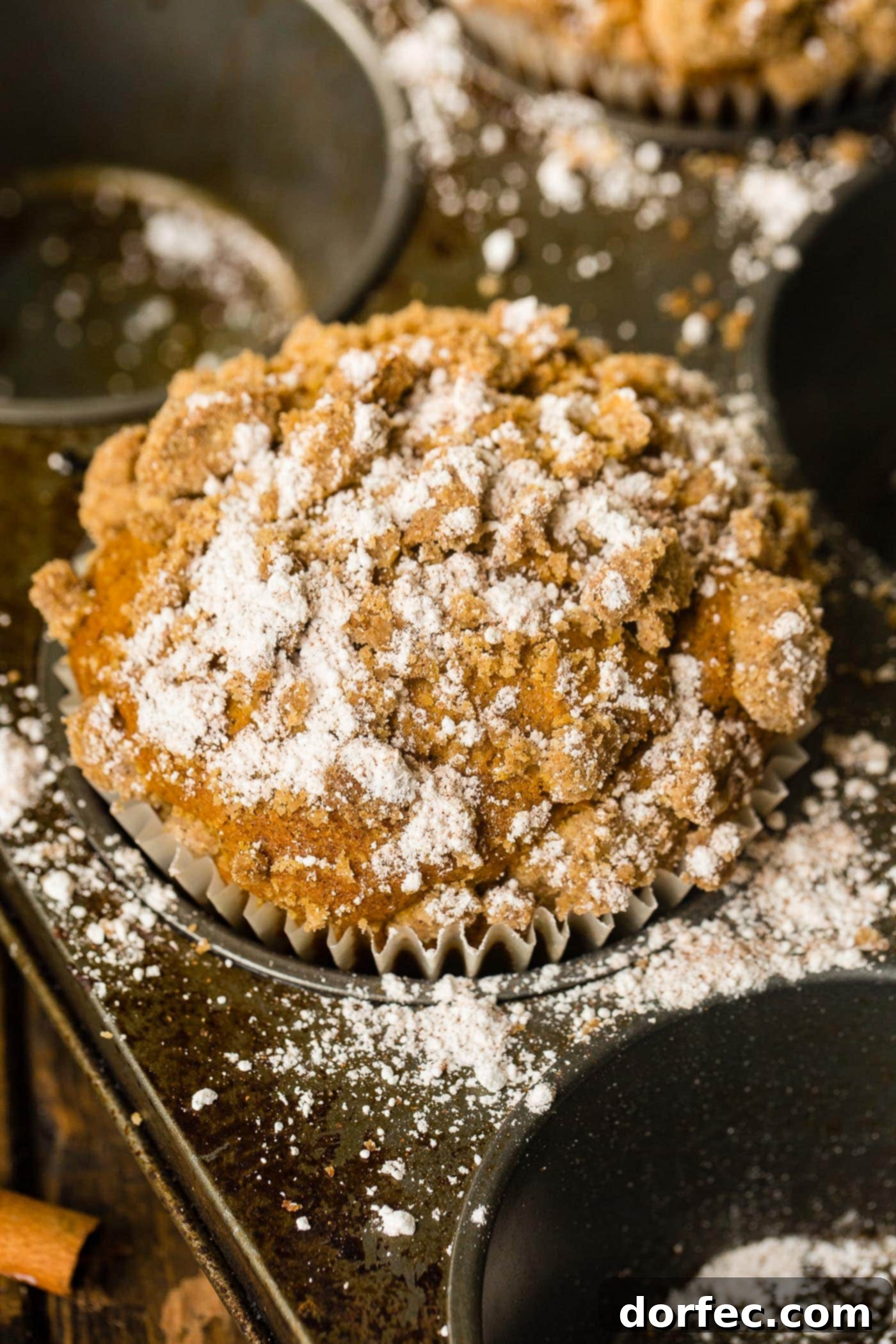 A vibrant, large pumpkin streusel muffin, delicately dusted with powdered sugar, set against a warm, inviting backdrop.