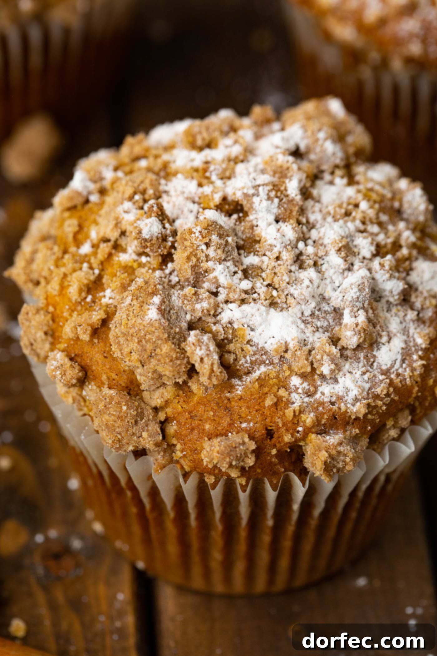 A close-up of a generously sized pumpkin streusel muffin, dusted with powdered sugar, highlighting its appealing texture.
