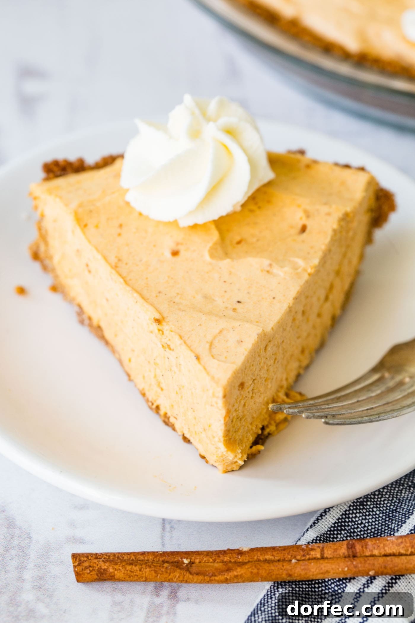 Marshmallow No Bake Pumpkin Pie A photo of a slice of no bake pumpkin pie with a swirl of whipped cream on top, presented beautifully on a white plate, ready for a festive table.