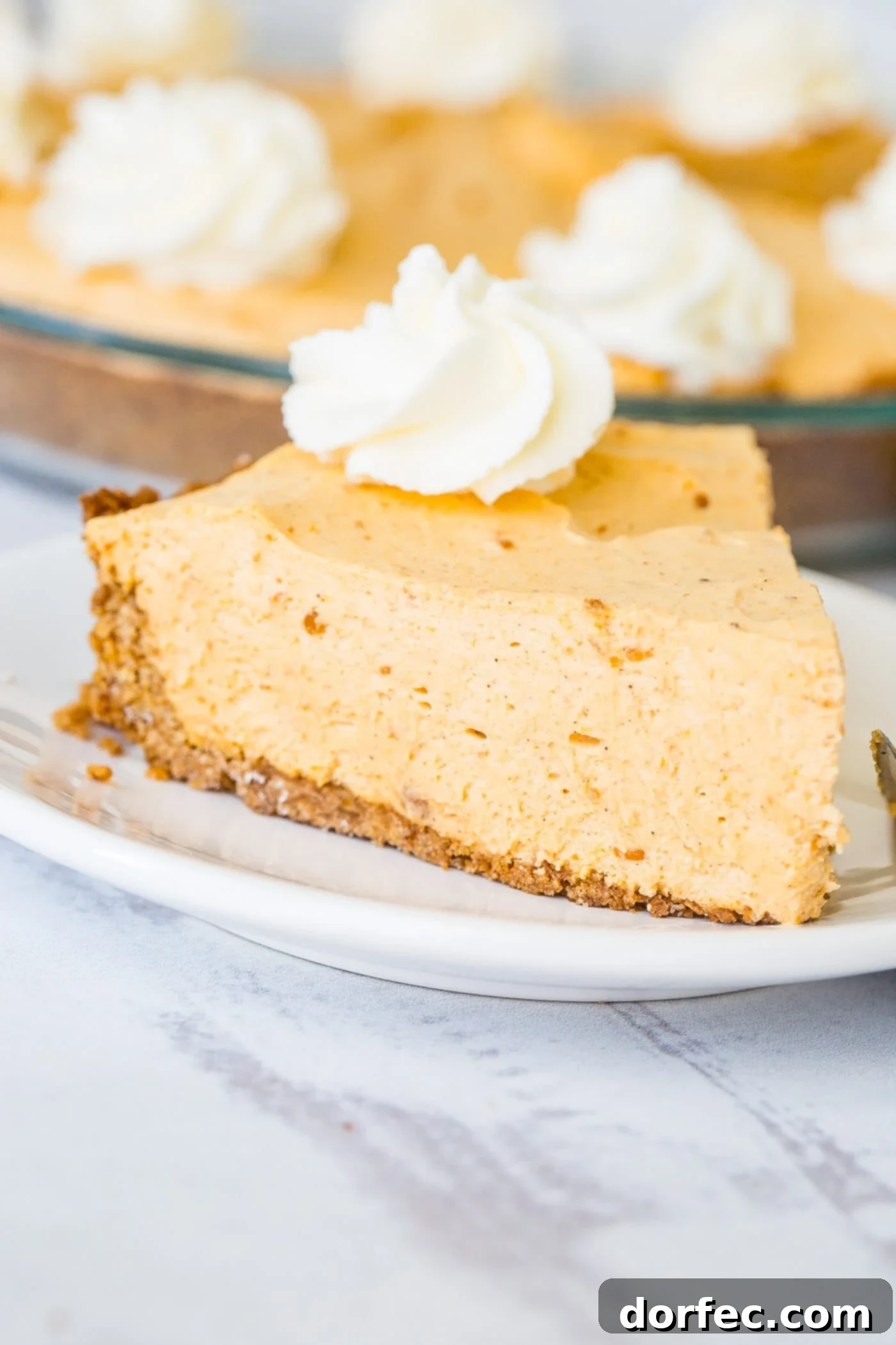 Marshmallow No Bake Pumpkin Pie A close-up photo of a decadent slice of no bake pumpkin pie on a white plate with a generous swirl of whipped cream on top, perfectly ready to be savored.