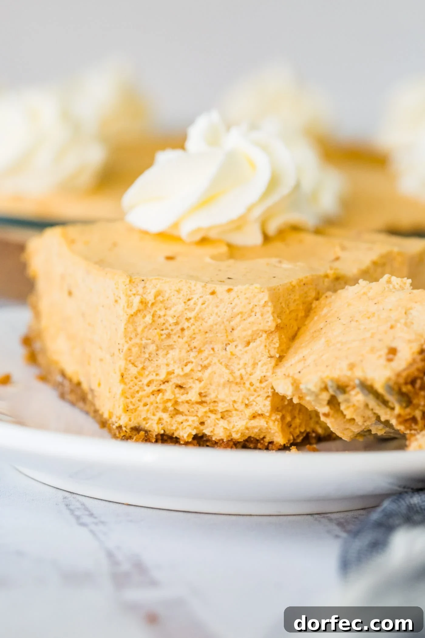 Marshmallow No Bake Pumpkin Pie A close-up photo of a slice of no bake pumpkin pie sitting on a white plate with a bite-size piece expertly removed with a fork, showcasing its luscious, creamy texture.