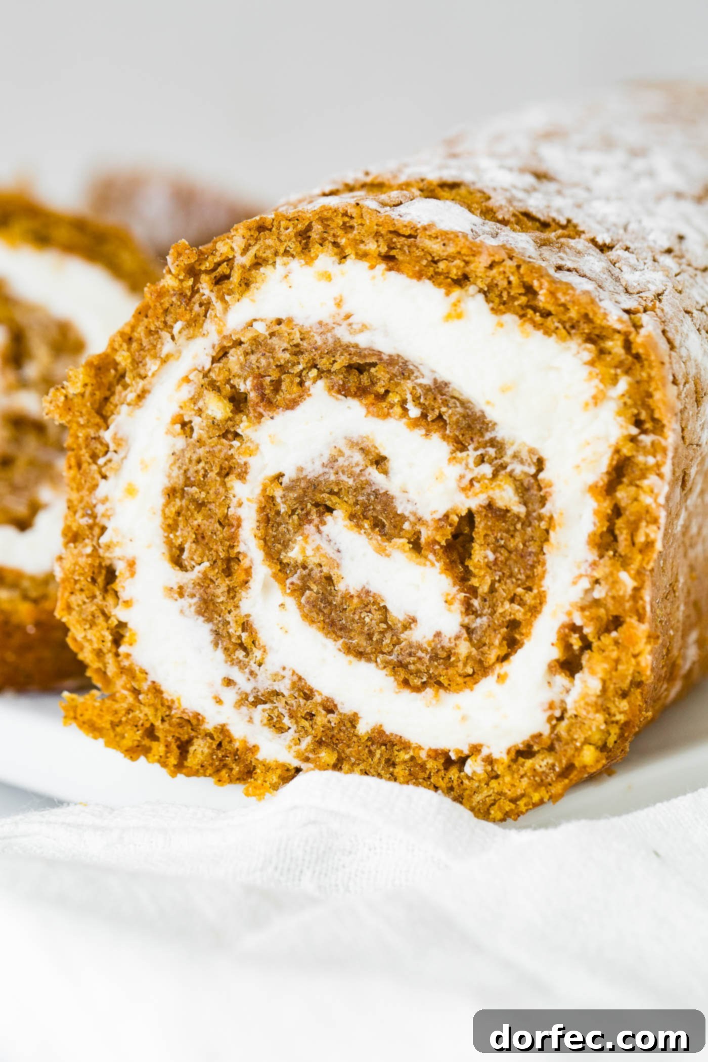 A close-up photo showing a perfect cross-section of a homemade pumpkin roll, revealing its tender cake and creamy filling.
