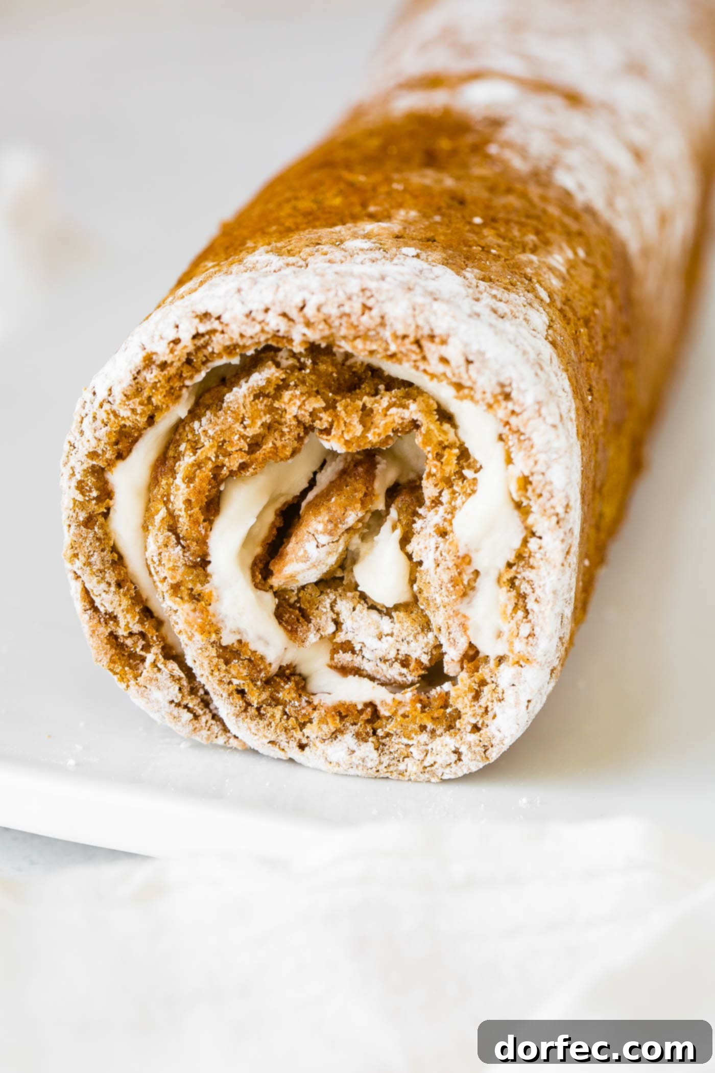 A rustic shot of a freshly rolled pumpkin cake, still wrapped in its powdered sugar-dusted towel, cooling on a wire rack.