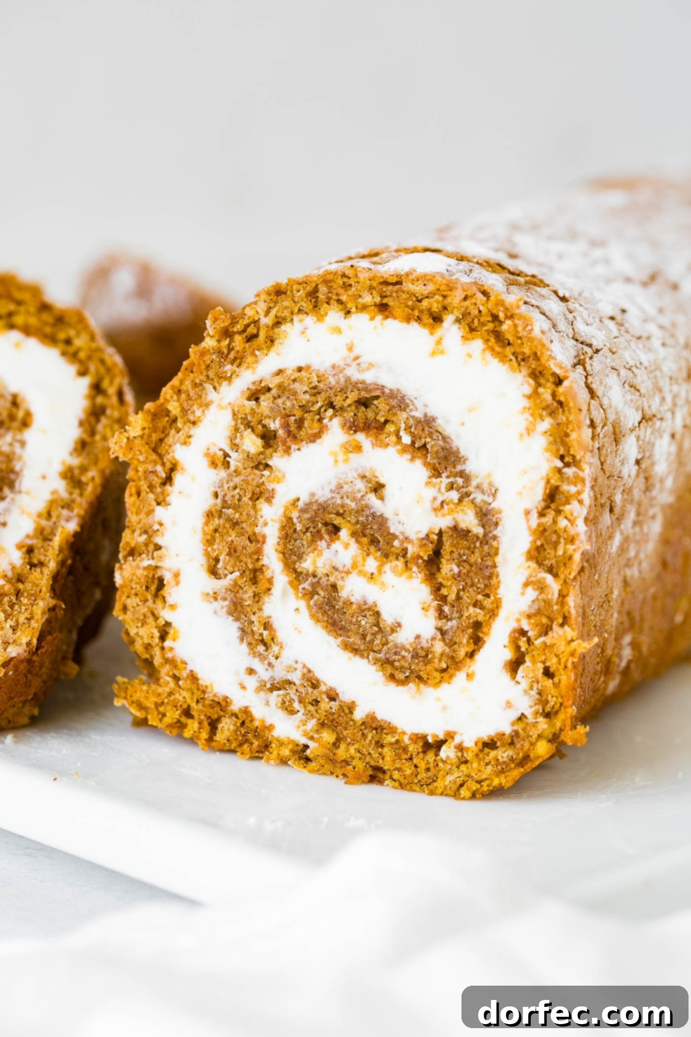 An enticing close-up of a pumpkin roll, sliced to reveal its moist cake and thick layer of cream cheese filling in a perfect spiral.
