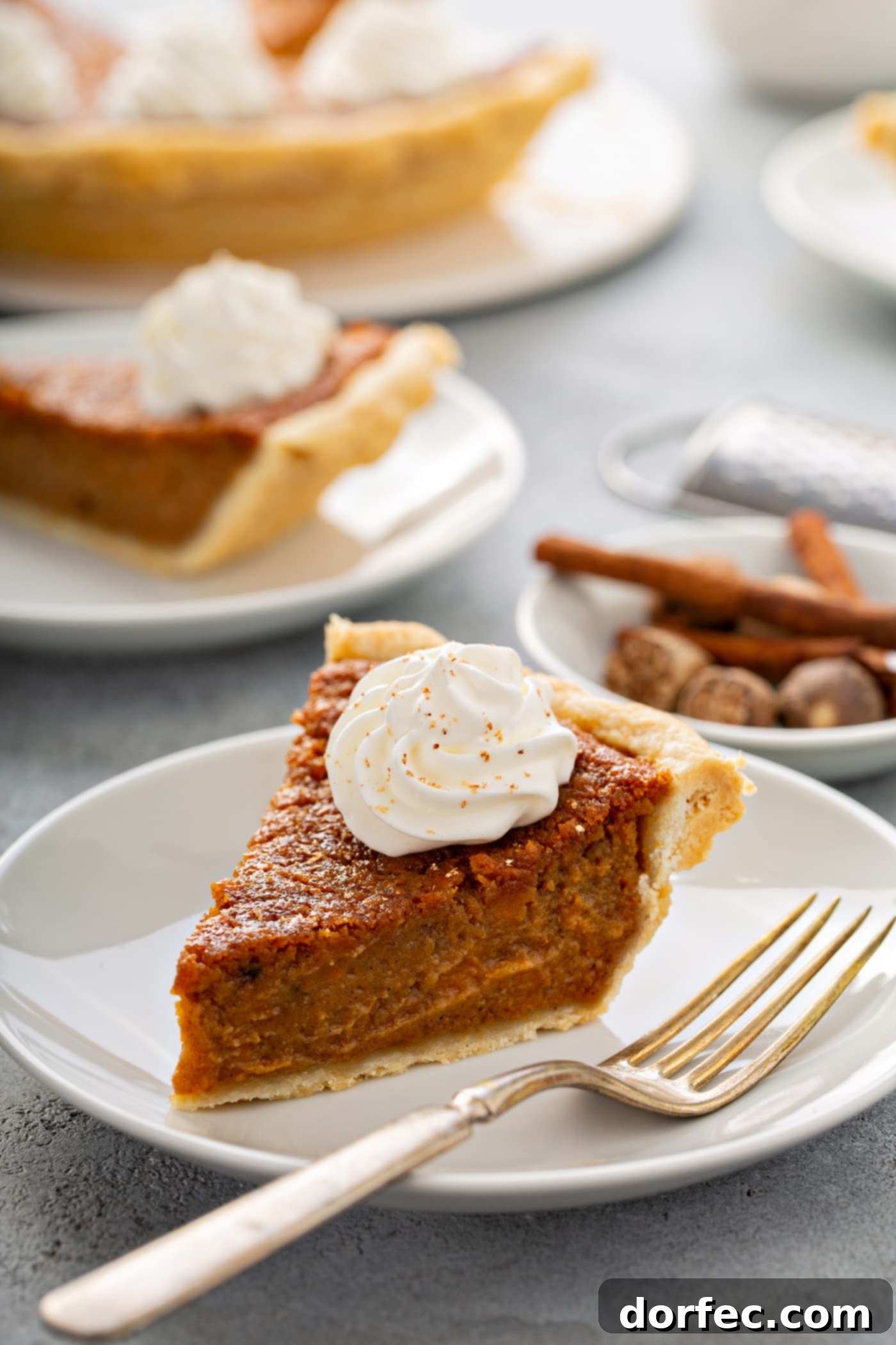 Southern Charm Sweet Potato Pie 13 A photo of a slice of sweet potato pie sitting on a white plate with a fork sitting next to it and other servings of pie in the background.
