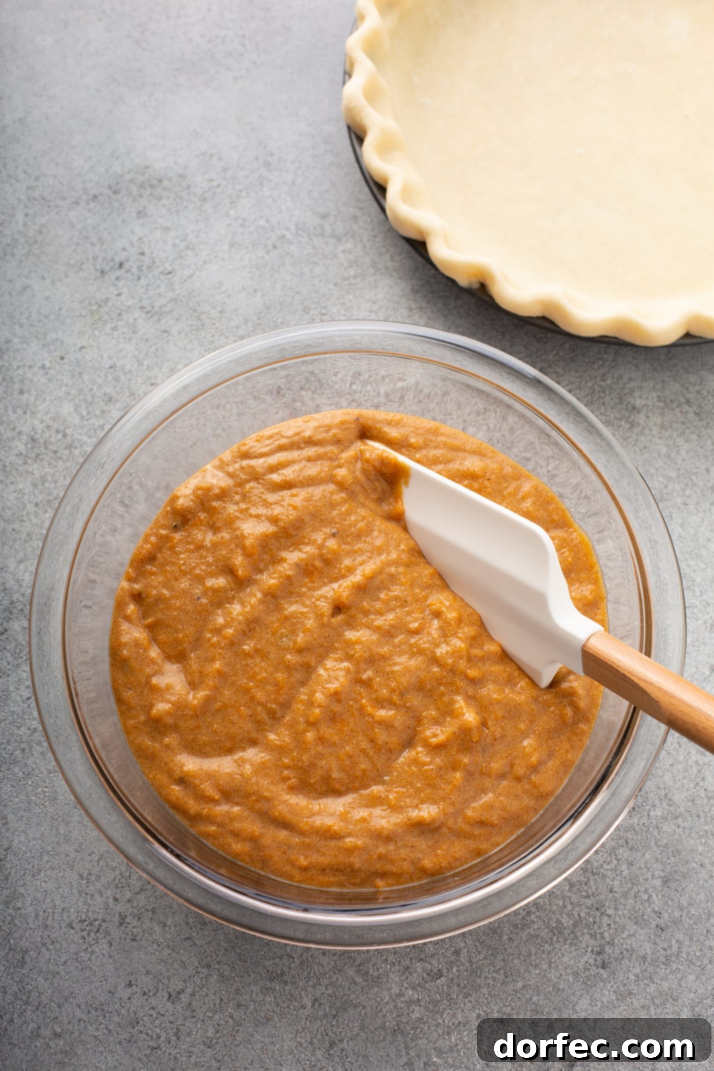 Southern Charm Sweet Potato Pie 4 A photo of a glass bowl full of sweet potato pie filling with a rubber spatula in it. The bowl is sitting next to an empty pie crust.