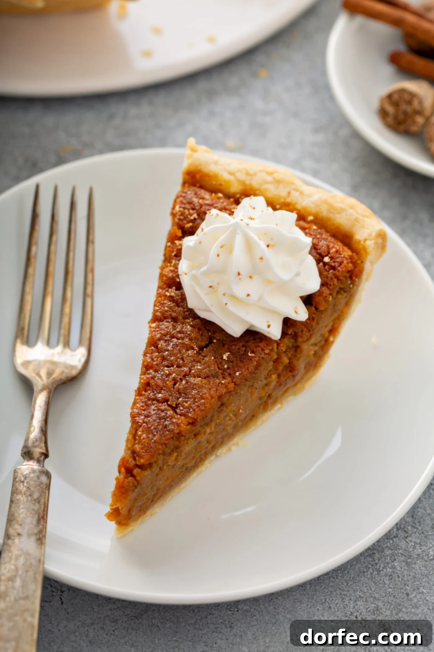 Southern Charm Sweet Potato Pie 9 A photo of a slice of sweet potato pie sitting on a white plate with a silver fork sitting next to it.