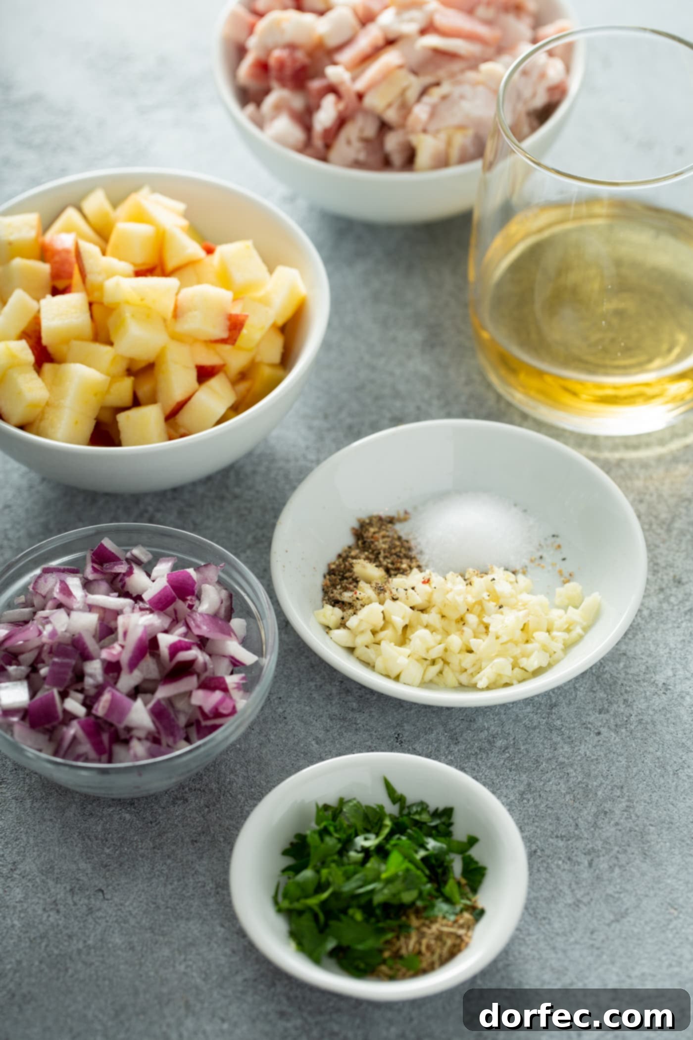 5 Small bowls containing cubed apples, chopped red onions, minced garlic and salt and pepper, apple juice, and minced parsley and sage.