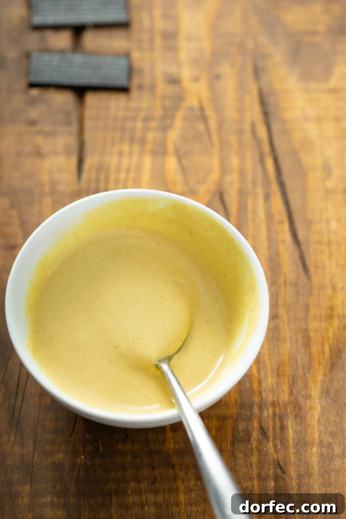 A bowl of maple mustard sauce with a spoon in it.