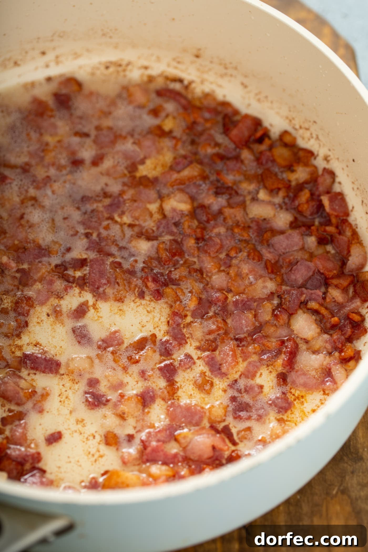 A skillet containing sizzling, chopped bacon.
