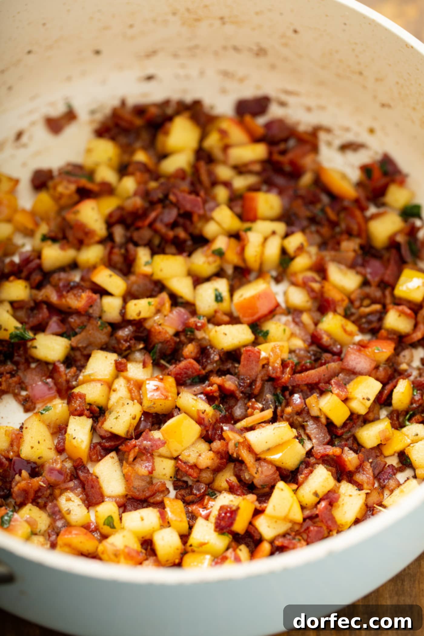 A skillet filled with cooked bacon, apples, onions, spices,and herbs.