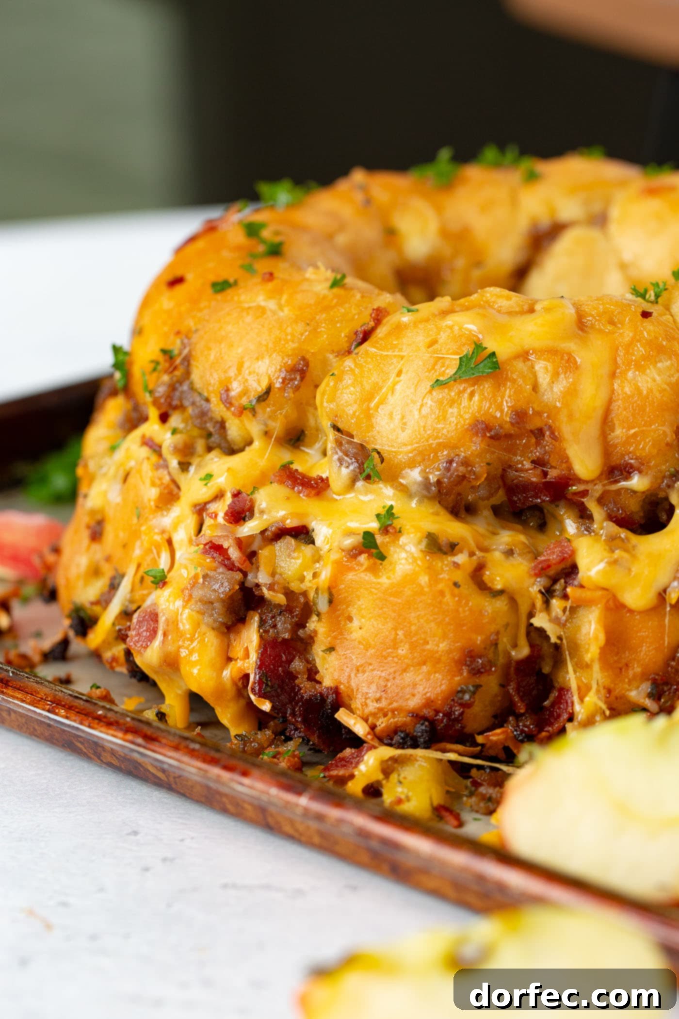 Breakfast Sausage and Apple Cheesy Pull Apart Close-up of golden-brown Breakfast Cheesy Pull Apart Bread on a platter, covered in melted cheddar cheese, with visible pieces of breakfast sausage, crispy bacon, and tender apple chunks peeking through.
