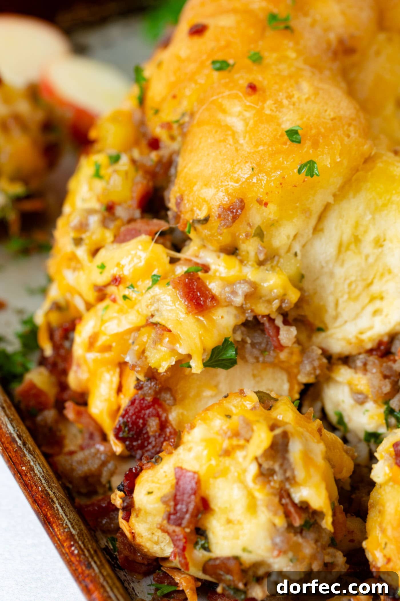 Breakfast Sausage and Apple Cheesy Pull Apart Delicious Cheesy Pull Apart Bread topped with abundant melted cheese, showcasing visible pieces of crispy bacon, savory sausage, and tender apples embedded within the golden-baked bread.