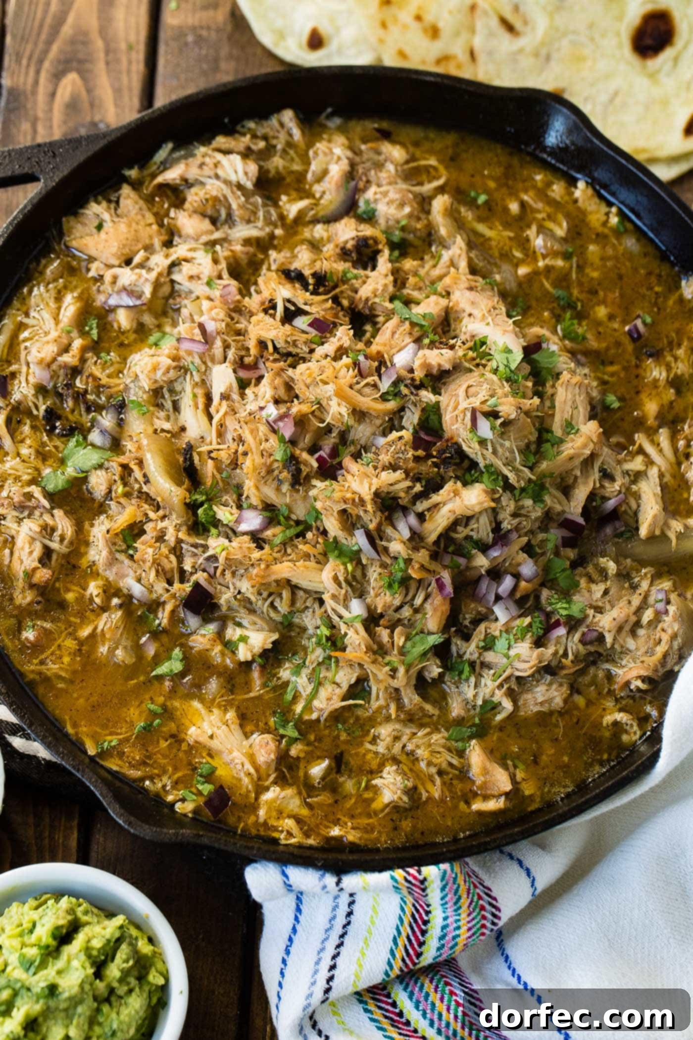 A photo of juicy crispy chicken carnitas in a cast iron skillet garnished with chopped cilantro and diced red onion.