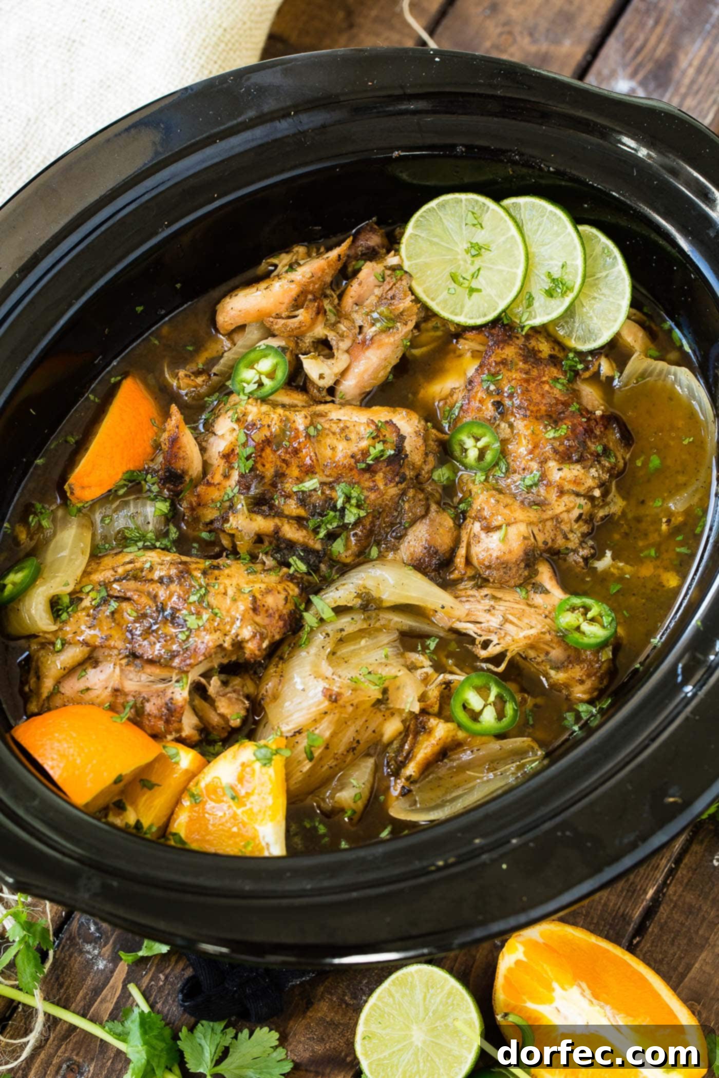 A photo of chicken carnitas being cooked in a slow cooker witl slices of fresh lime.