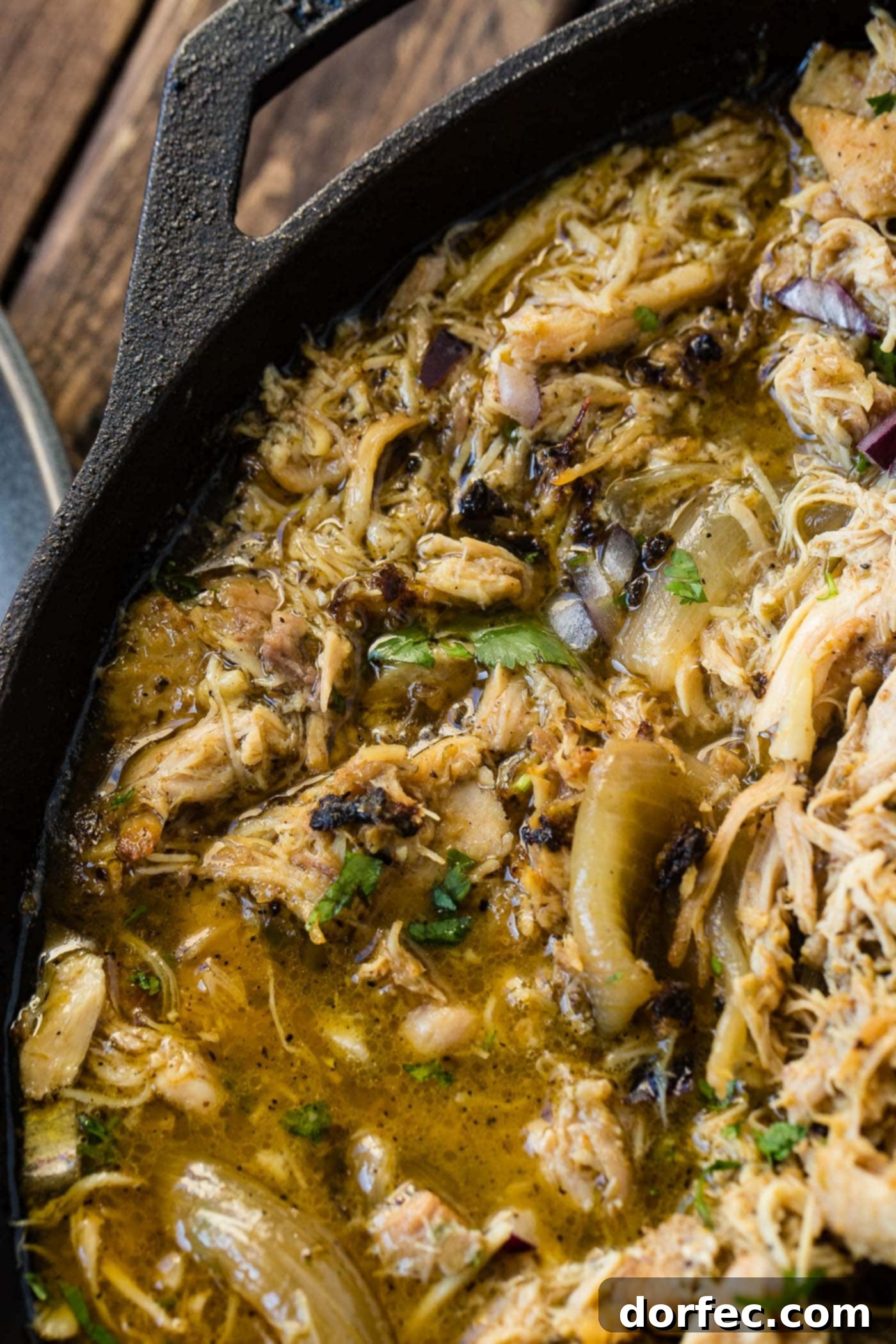 A photo of juicy crispy chicken carnitas in a cast iron skillet garnished with chopped cilantro and diced red onion.