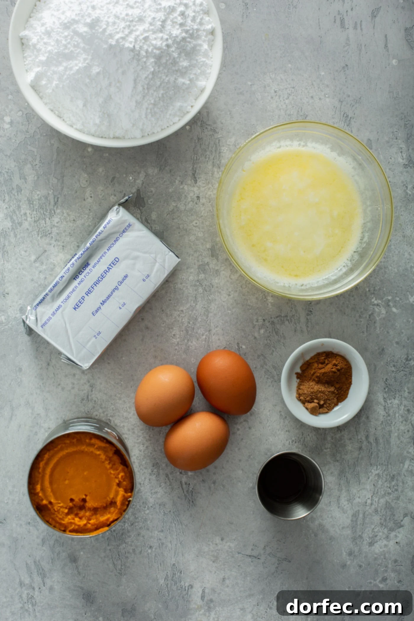 Key Ingredients for Paula Deen's Pumpkin Gooey Butter Cake Ingredients for pumpkin gooey butter cake, including bowls of cake mix, melted butter, cinnamon, vanilla, three brown eggs, a can of pumpkin, and cream cheese.