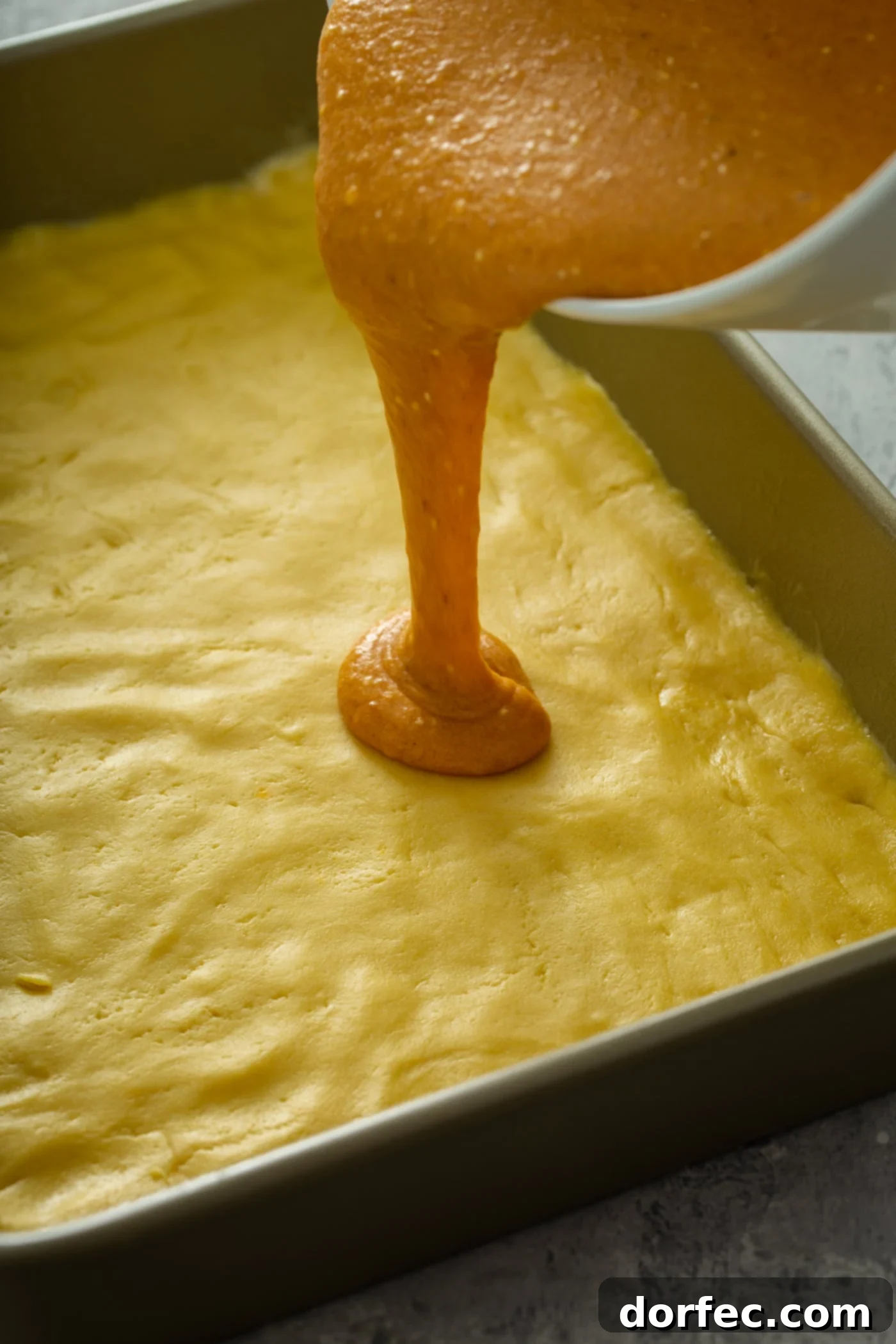Pouring the Creamy Pumpkin Filling Over the Crust Pumpkin mixture being poured over yellow cake mix crust, preparing for baking.