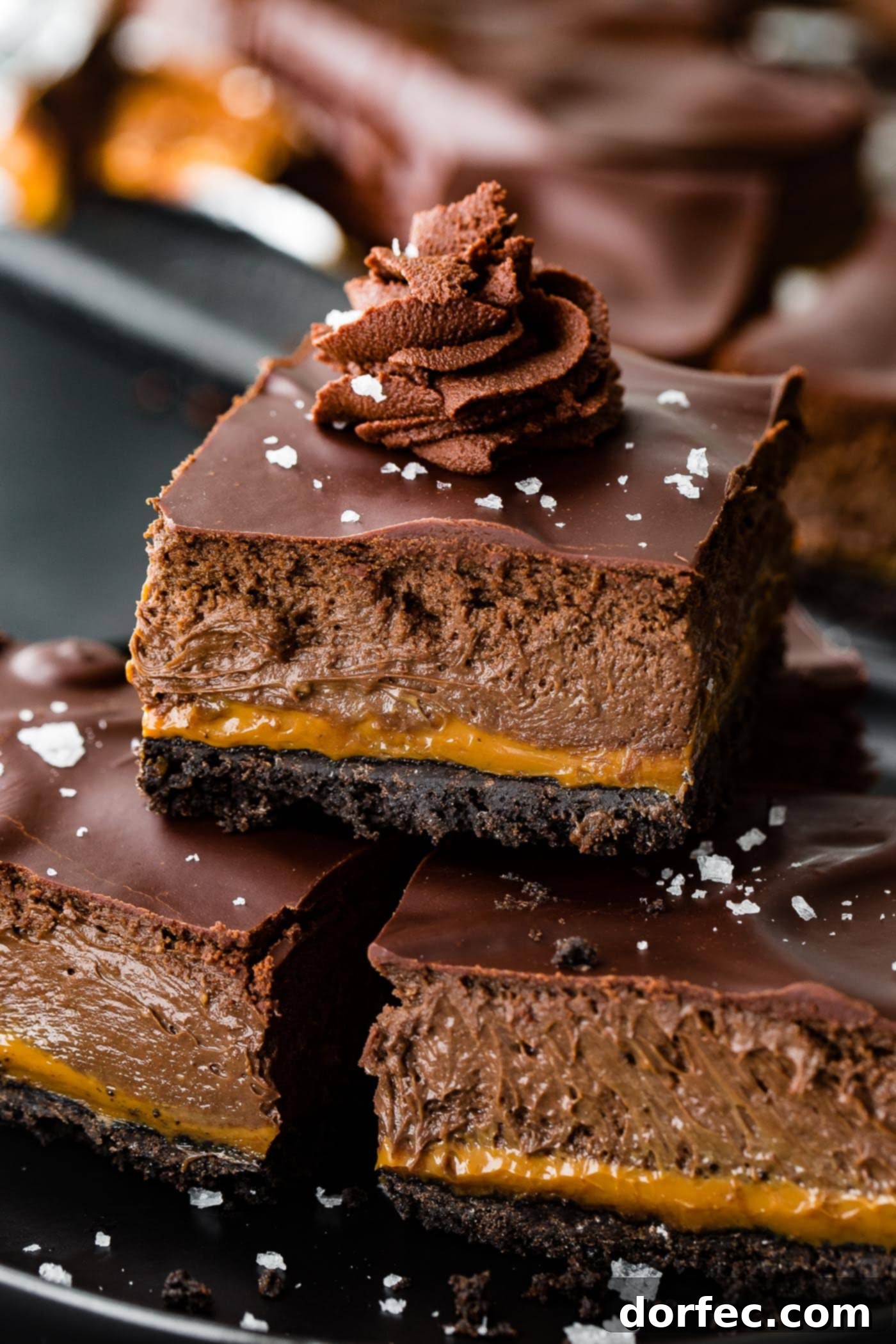A trio of layered gooey cream cheese dessert bars with whipped ganache and sea salt on top, showing their rich texture.