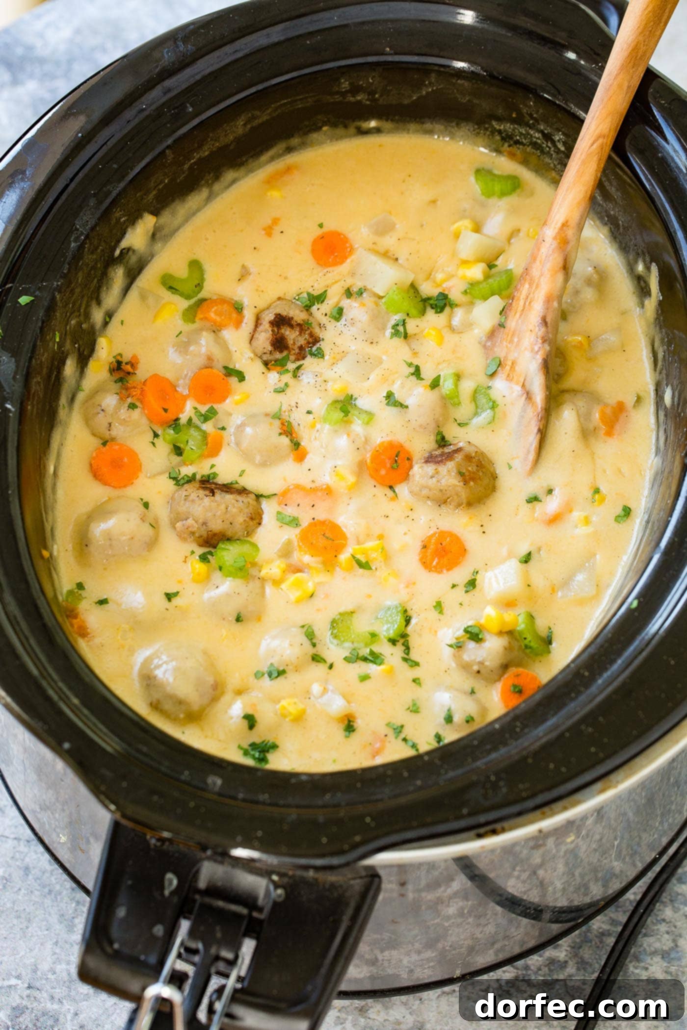A slow cooker filled with a creamy, golden cheesy meatball soup, rich with tender meatballs, vibrant carrots, hearty potatoes, and crisp celery. Perfect for a cozy meal.