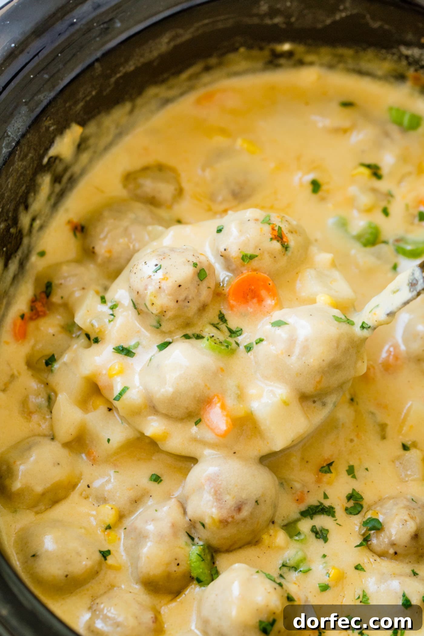 Close-up shot of the creamy cheesy meatball soup in a slow cooker, showcasing the perfectly melted cheese coating the meatballs, carrots, potatoes, and celery. A truly indulgent comfort food.