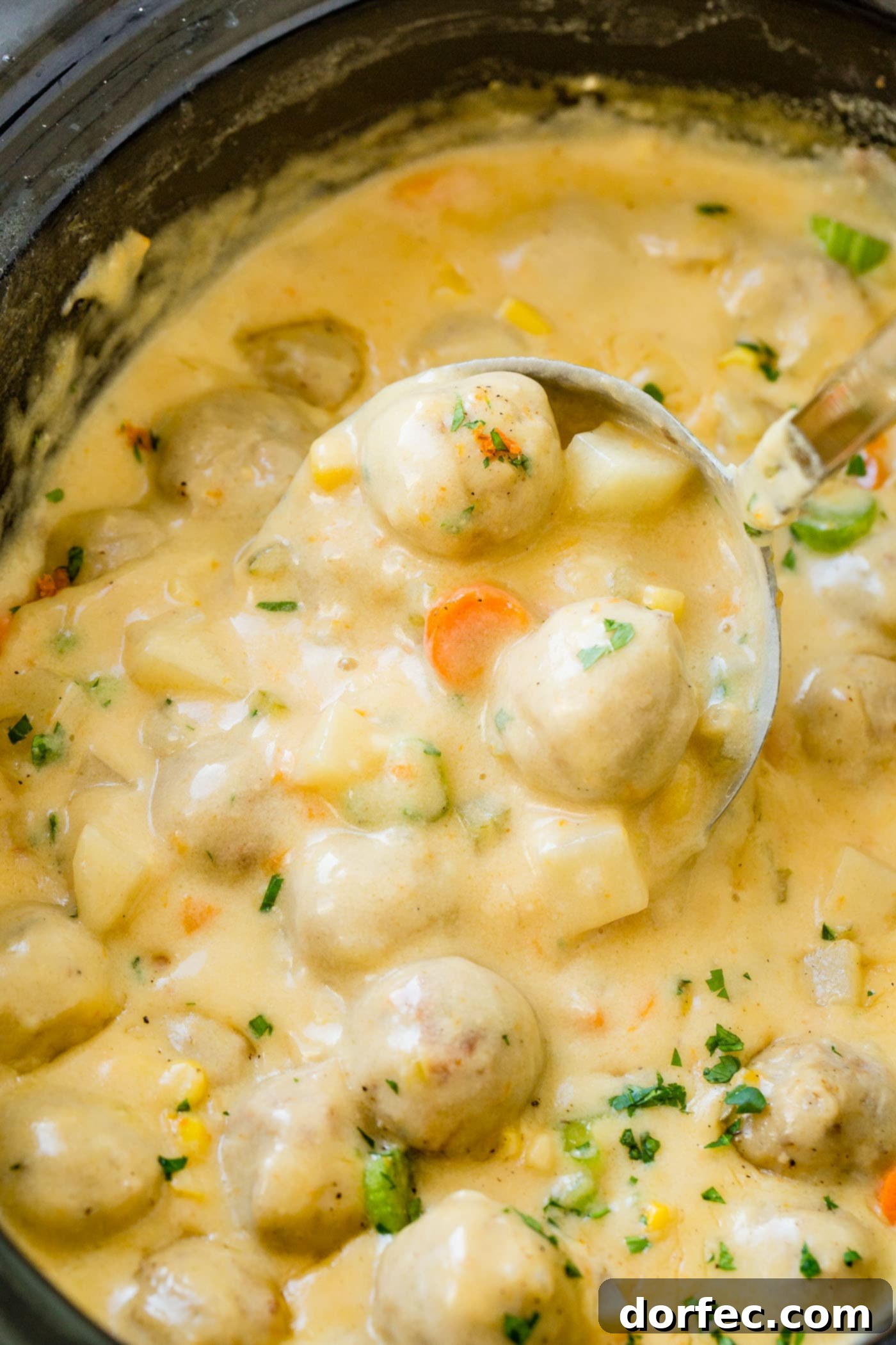 A slow cooker filled with the inviting Cheesy Meatball Soup, rich with tender meatballs, carrots, potatoes, and celery, ready to provide warmth and comfort on a cool day.