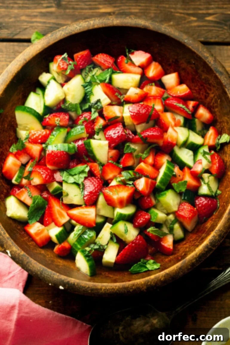 Honey Balsamic Strawberry Cucumber Salad 2 A beautifully presented wooden serving bowl brimming with fresh strawberry cucumber salad, garnished with vibrant mint leaves.