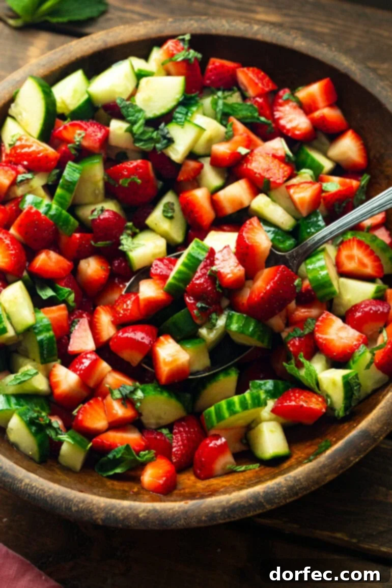Honey Balsamic Strawberry Cucumber Salad 3 A large metal spoon gently stirring a vibrant cucumber strawberry salad in a wooden serving bowl, showcasing the fresh ingredients.