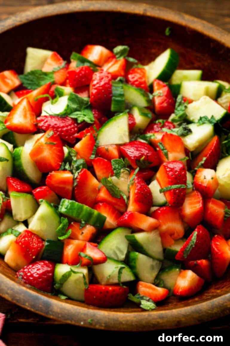 Honey Balsamic Strawberry Cucumber Salad 5 A close-up shot of refreshing cucumber strawberry salad mixed with vibrant fresh mint leaves in a bowl.