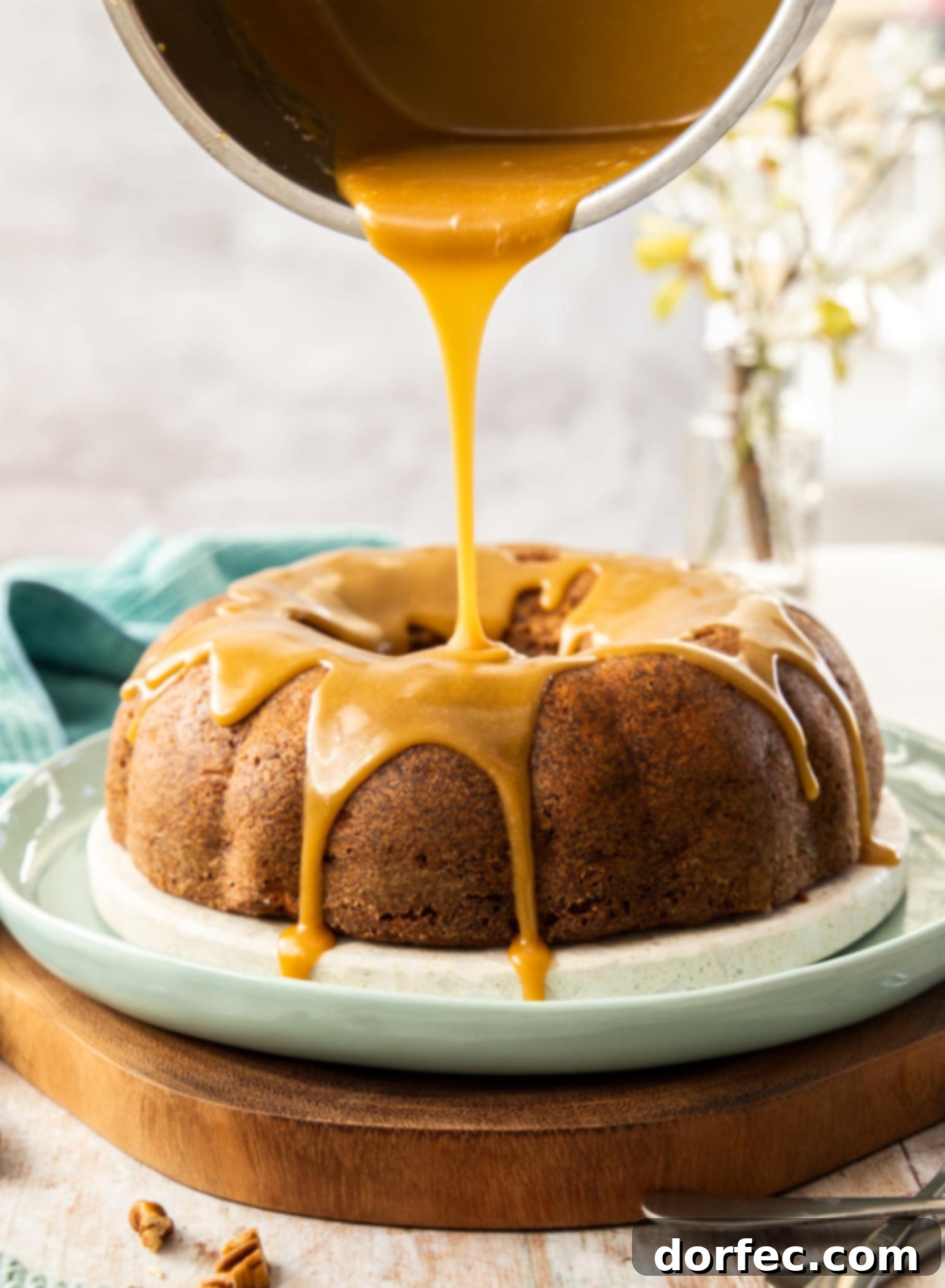 Caramel sauce being carefully poured from a saucepan, creating beautiful drips over a freshly baked apple cinnamon bundt cake, signifying pure indulgence.