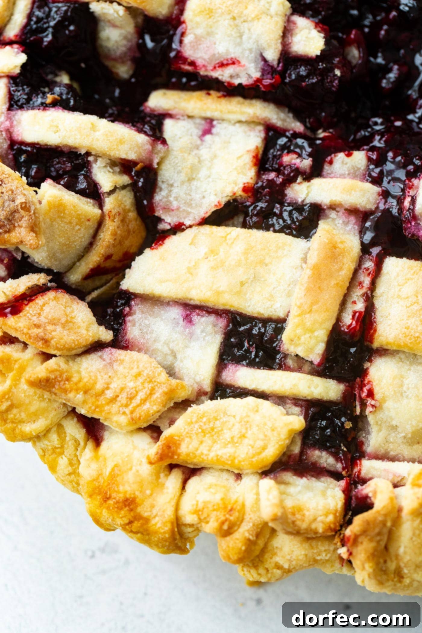 A close-up view of a golden, lattice-topped Marionberry pie, perfectly baked with its rich, dark filling bubbling underneath.