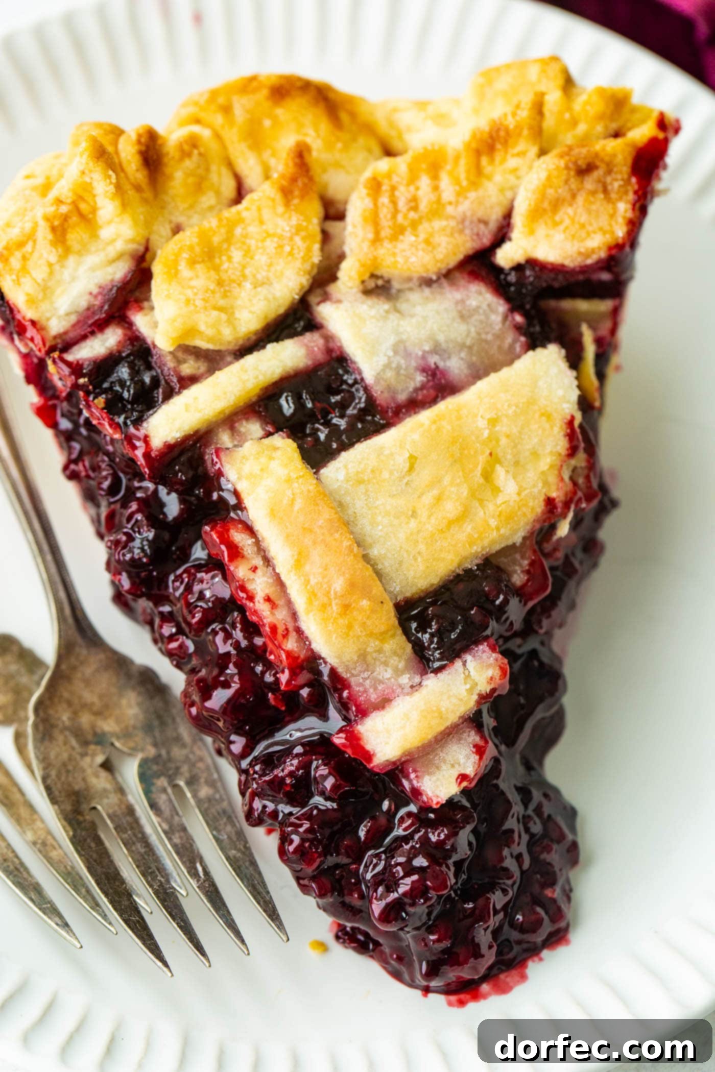A final, mouth-watering slice of Marionberry pie resting on a pristine white plate, with two forks poised, inviting a taste.
