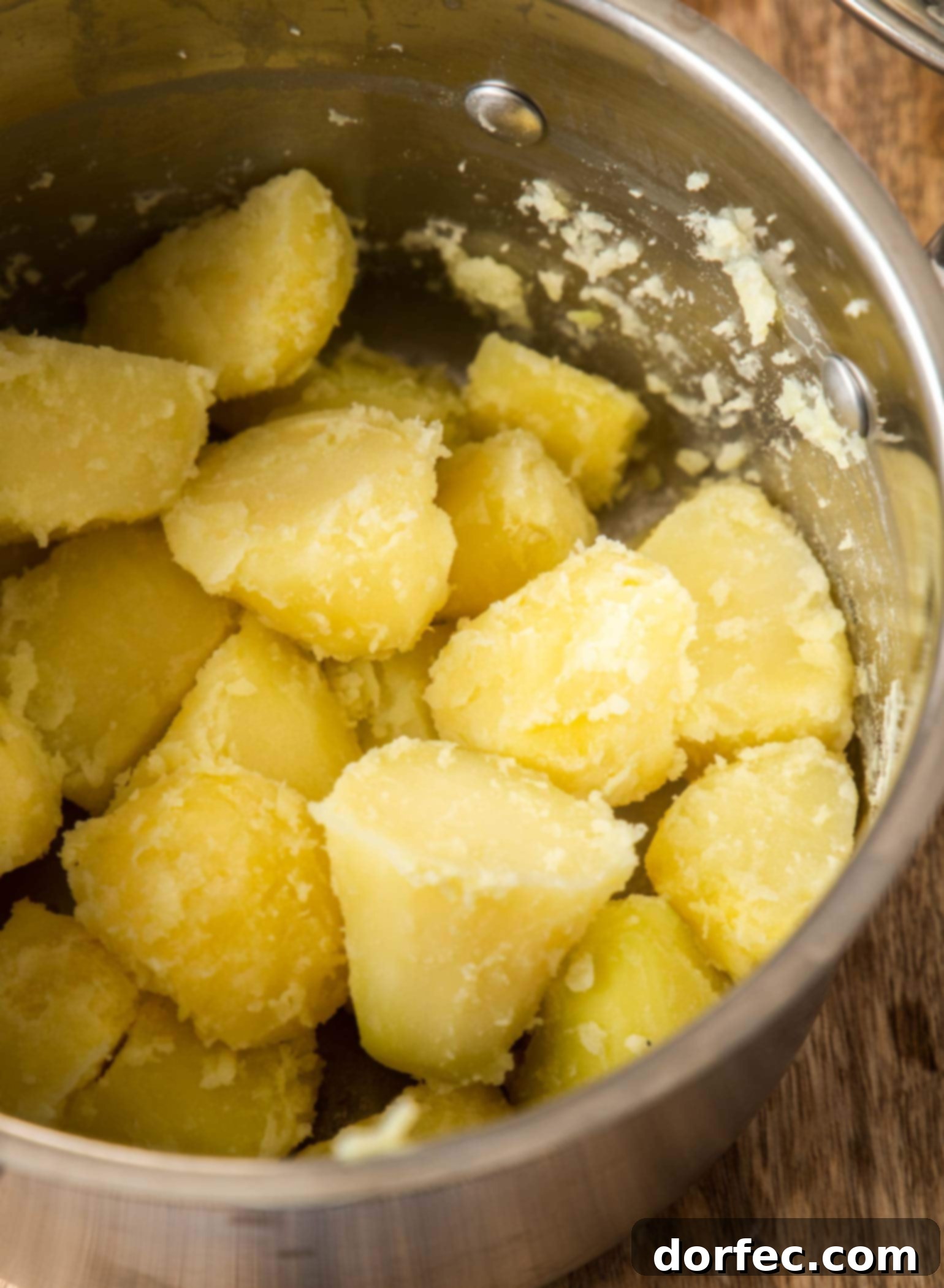 A saucepan filled with par-boiled Yukon Gold potatoes, roughed up and ready for roasting, sitting on a wooden surface.