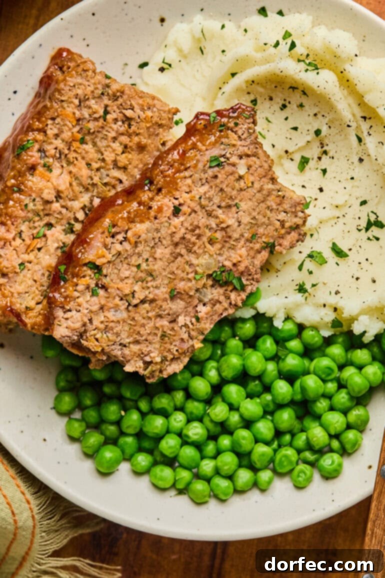 Two slices of classic meatloaf served on a plate with creamy mashed potatoes and vibrant green peas, ready to be enjoyed.