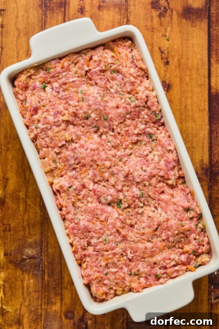 The first layer of glaze brushed evenly over the top of the raw meatloaf in the pan.
