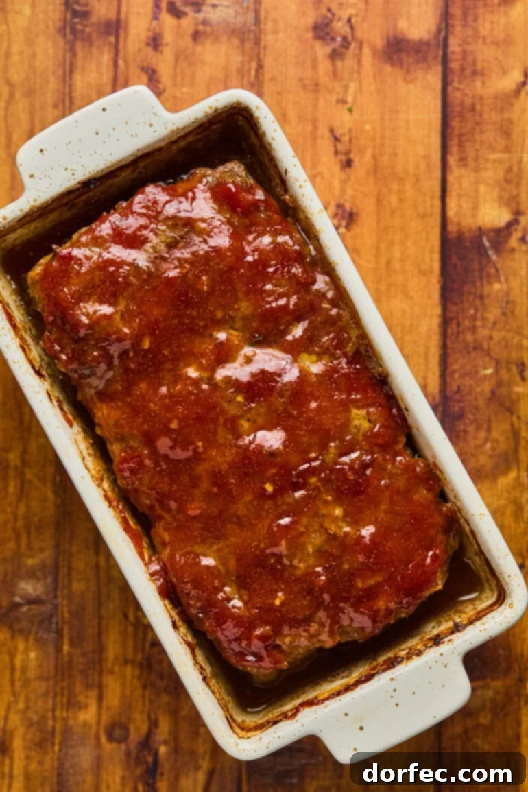 The second layer of glaze being brushed onto the partially baked meatloaf, creating a rich, glossy finish.