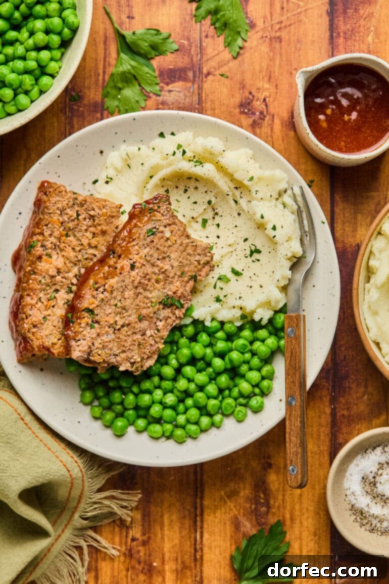 A hearty dinner plate featuring two generous slices of homemade classic meatloaf, accompanied by creamy mashed potatoes and a serving of vibrant green peas.