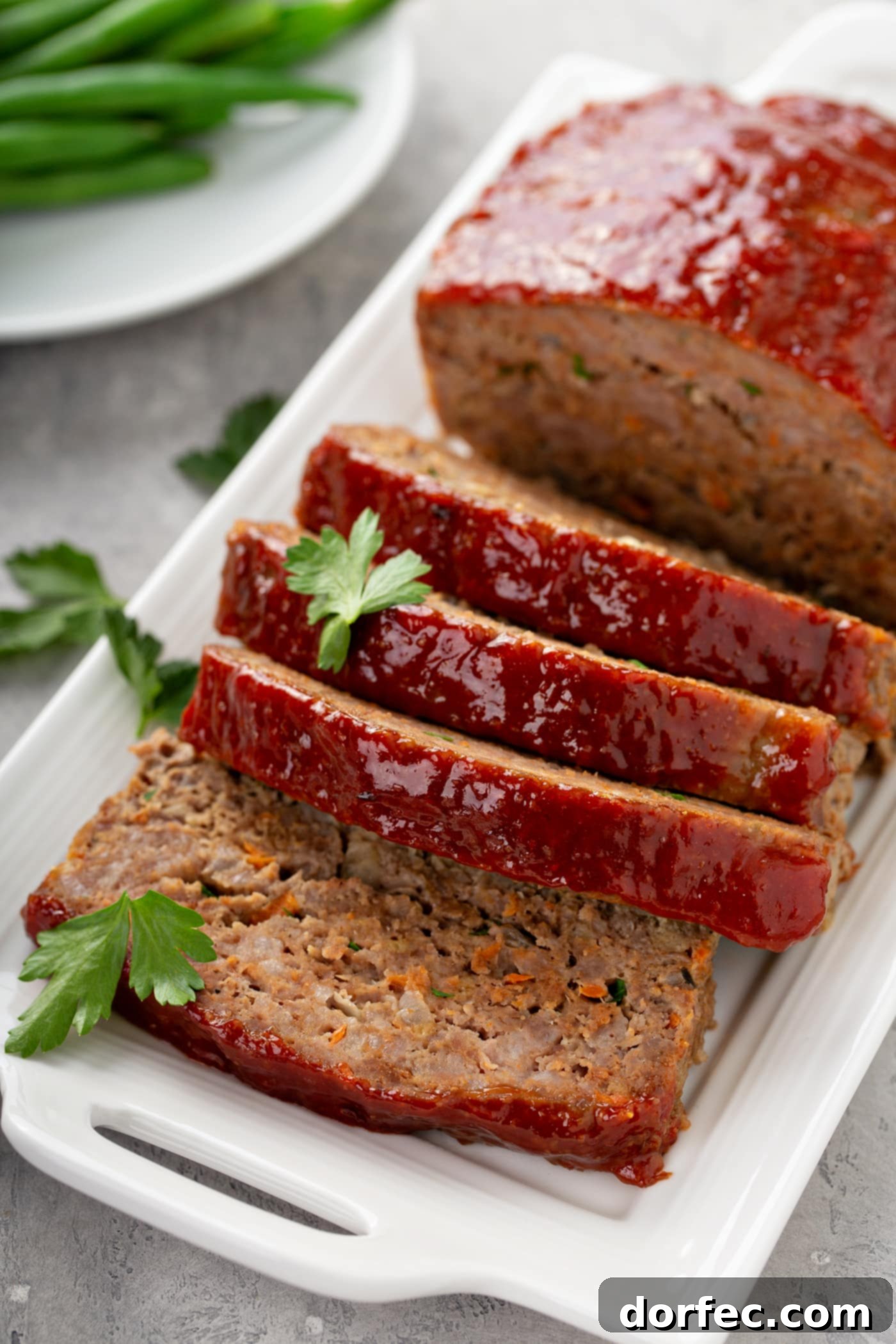 A beautiful meatloaf, freshly baked and partially sliced, presented on a platter with fresh parsley garnish, ready to be served.