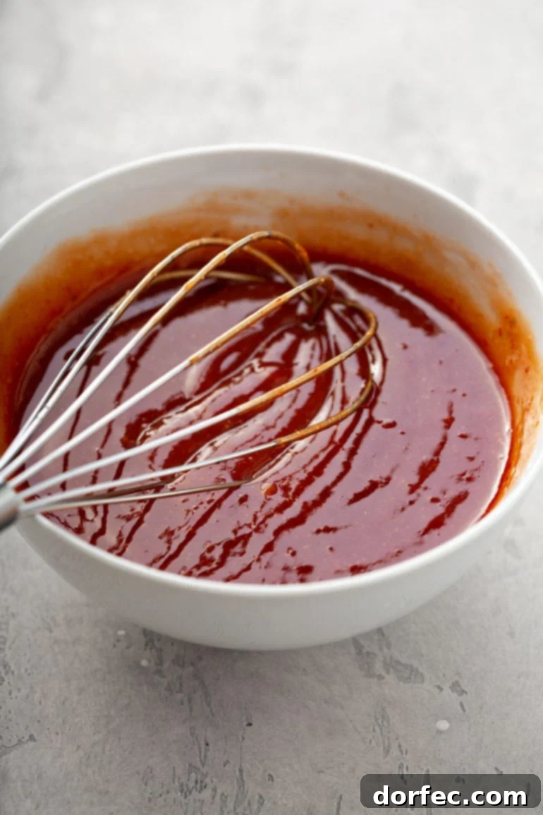 A glistening bowl of homemade meatloaf glaze, a perfect blend of ketchup, Worcestershire sauce, chili sauce, vinegar, and brown sugar, with a whisk resting in it.