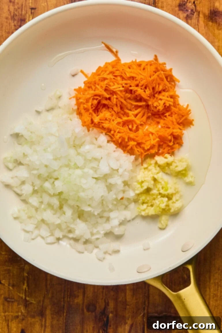 Close-up of a skillet with sautéing onions, carrots, and garlic, turning translucent and fragrant for the meatloaf base.