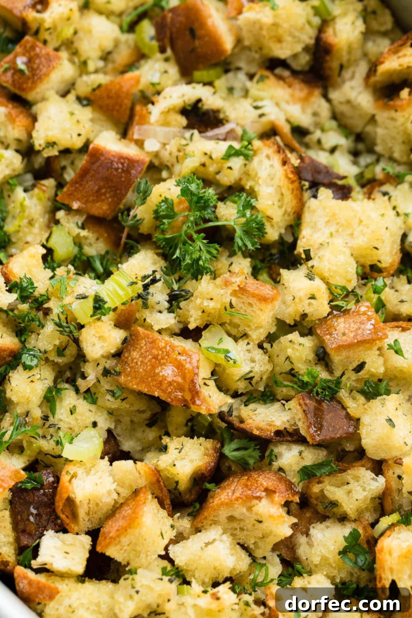 A close up photo of classic stuffing that is golden brown and topped with chopped fresh parsley, showcasing its crispy texture.